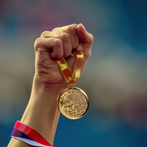 hand of a woman raising an Olympic gold medal in victory